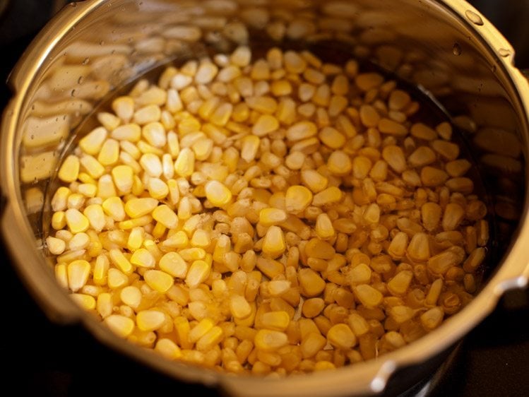 rinsed corn kernels, water and salt added in a pressure cooker for corn chaat recipe. 