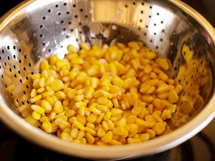 Sieben gekochter Maiskörner in einem Stahlsieb. 