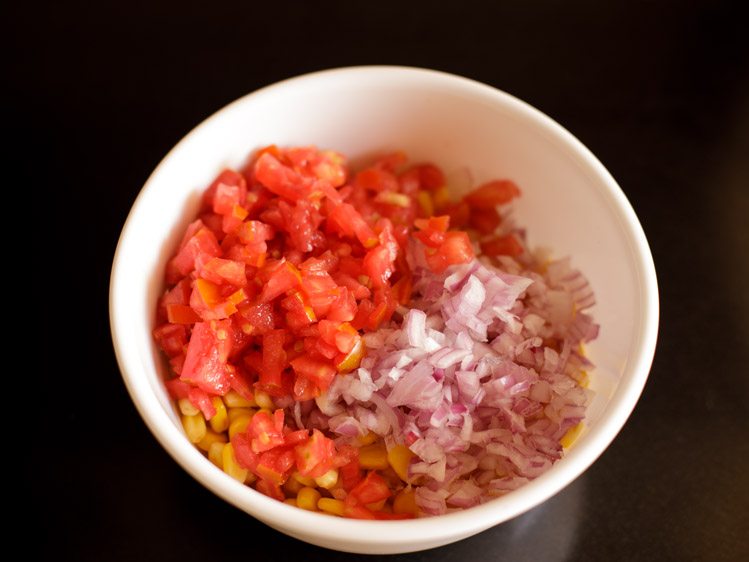 finely chopped onions and tomatoes added to the boiled corn kernels in the bowl. 