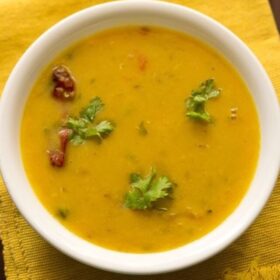masoor dal garnished with coriander leaves and served in a white bowl placed on a yellow kitchen cloth.