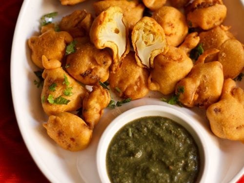 gobi pakora served on a white plate with green chutney.