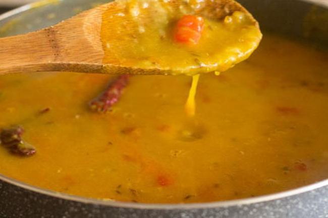 consistency of red lentils being shown with a wooden spoon.