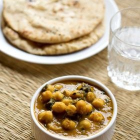 methi chole served in a bowl with naan and a glass of water.