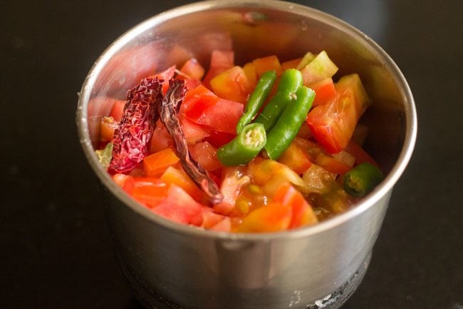 adding chopped tomatoes, chopped green chili and dried red chili to blender jar for tomato paste