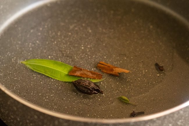 adding bay leaf, black cardamoms, green cardamoms, cinnamon and cloves to hot oil in pan