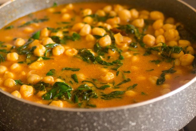 stirring chole and water in pan