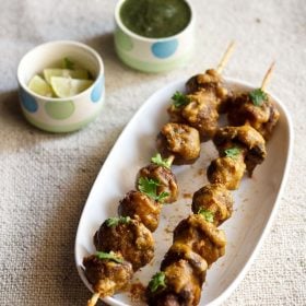 mushroom tikka served on a white platter with green chutney and lemon wedges kept in a small bowl on the top side.