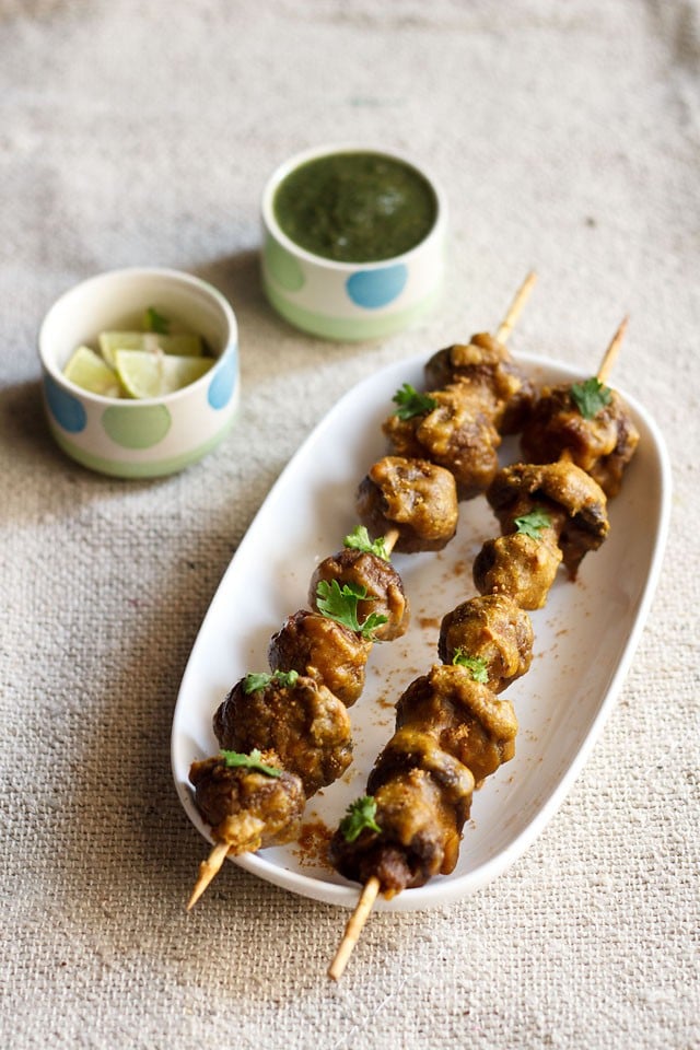 mushroom tikka served on a white platter with green chutney and lemon wedges kept in a small bowl on the top side.