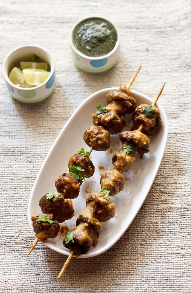 mushroom tikka served on a white platter with green chutney and lemon wedges kept in a small bowl on the top side. 