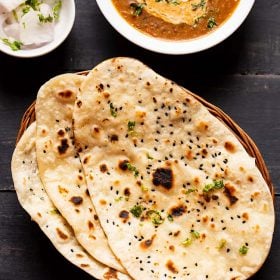 naan kept on top of each other in a cane basket. served with dal makhani in a white bowl and side of sliced onions garnished with coriander leaves in a small bowl.