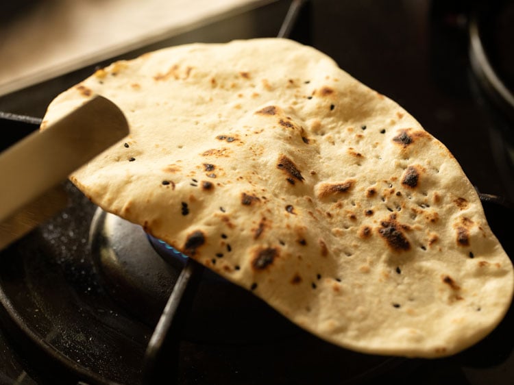 cooking naan bread on direct flame using tongs