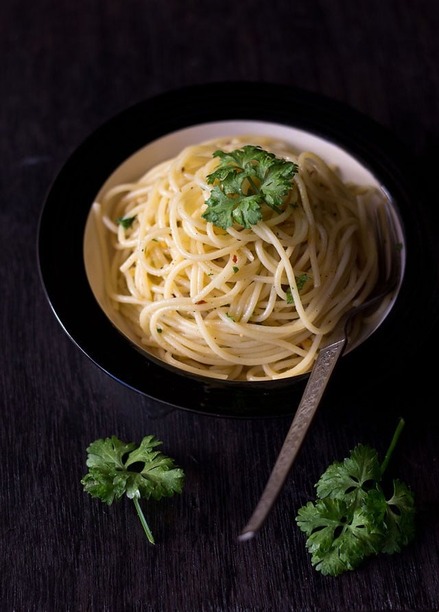 spaghetti aglio e olio garnished with parsley and served in a black rimmed white bowl with a fork kept on the right side.