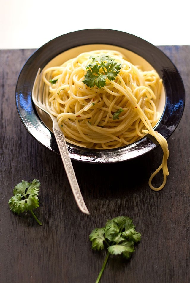 spaghetti olio e aglio garnished with parsley and served in a black rimmed white bowl with a fork kept in the left side.