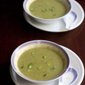 spring onion soup served in soup bowls placed on a plate with a spoon kept by the side.