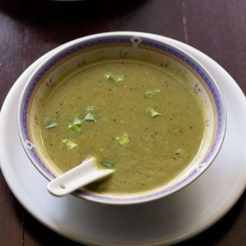 spring onion soup served in soup bowl placed on a plate with a spoon inside.