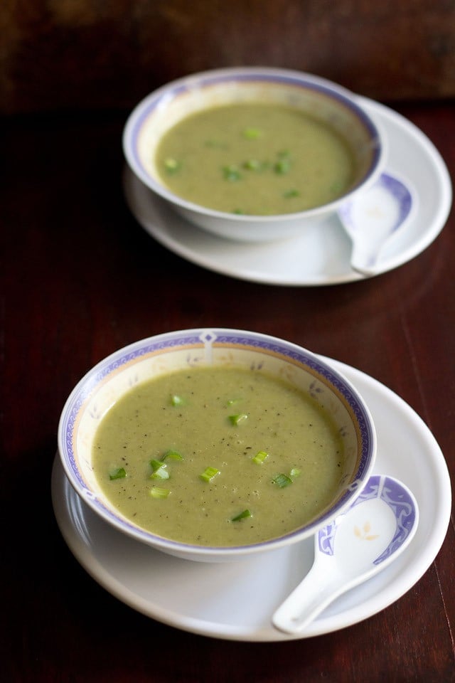 spring onion soup served in soup bowls placed on a plate with a spoon kept by the side.