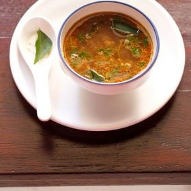 tamarind rasam served in a bowl on a white tray.