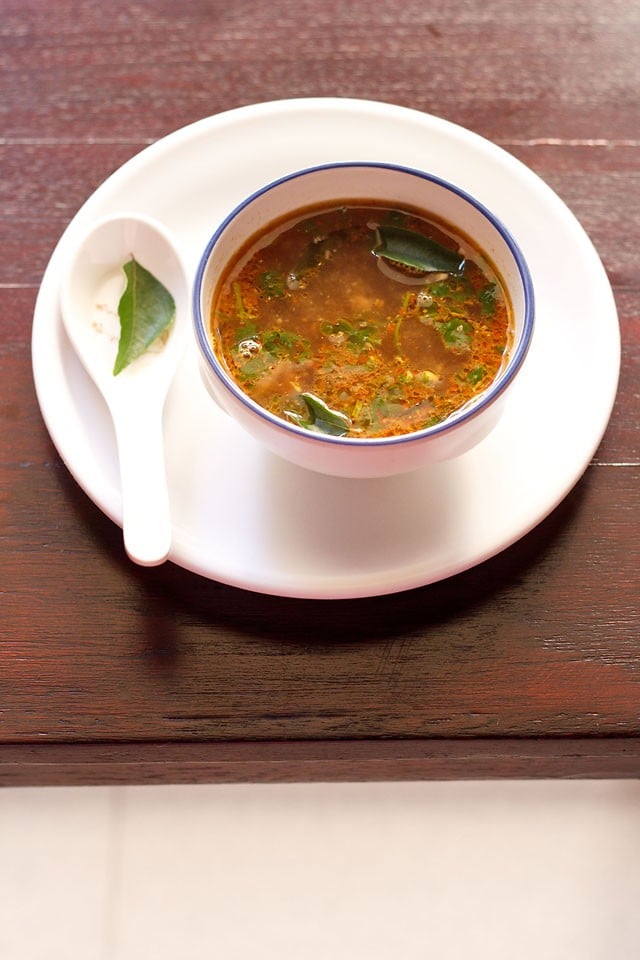 tamarind rasam served in a bowl on a white tray.