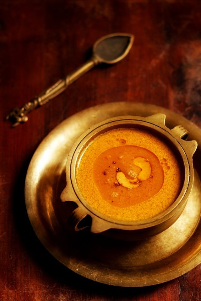 carrot payasam served in a brass bowl placed on a brass plate with a brass spoon kept on the top left side.