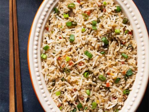 fried rice in an oval ceramic bowl with wooden chopsticks on a slate black board