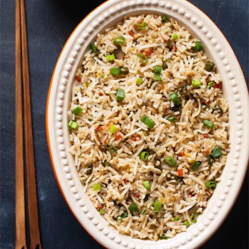 fried rice in an oval ceramic bowl with wooden chopsticks on a slate black board