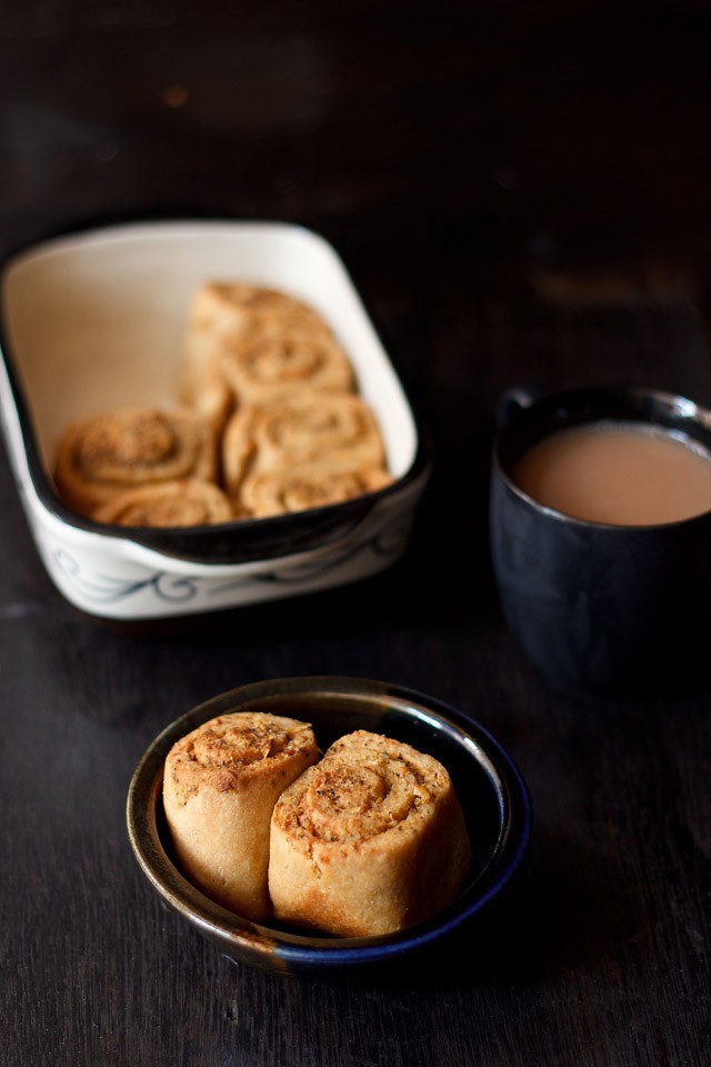 2 garlic bread rolls in a bowl on a black table with a black mug of tea.