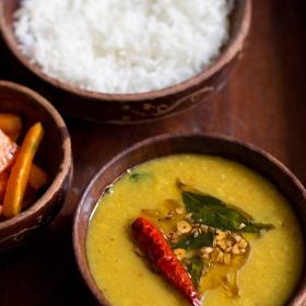 khatti dal with the tempering mix on top in a wooden bowl.