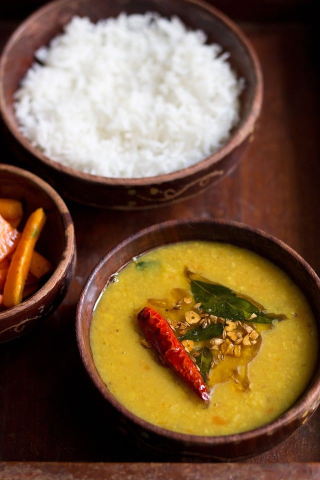 khatti dal with the tempering mix on top in a wooden bowl.