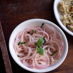 onion salad garnished with mint leaves and served in a white bowl.