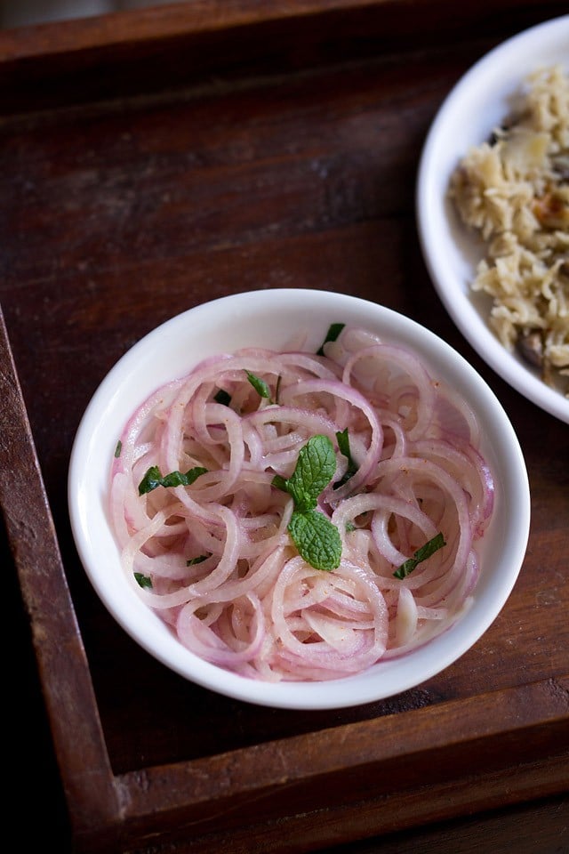 onion salad garnished with mint leaves and served in a white bowl.