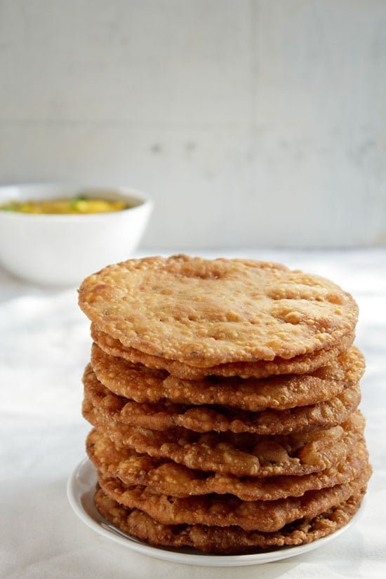 pakwans served on a white plate stacked on top of each other with a bowl of dal in the background. 