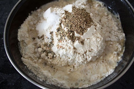 all purpose flour, whole wheat flour, carom seeds, cumin seeds, crushed black pepper, salt, oil and water added to a bowl. 