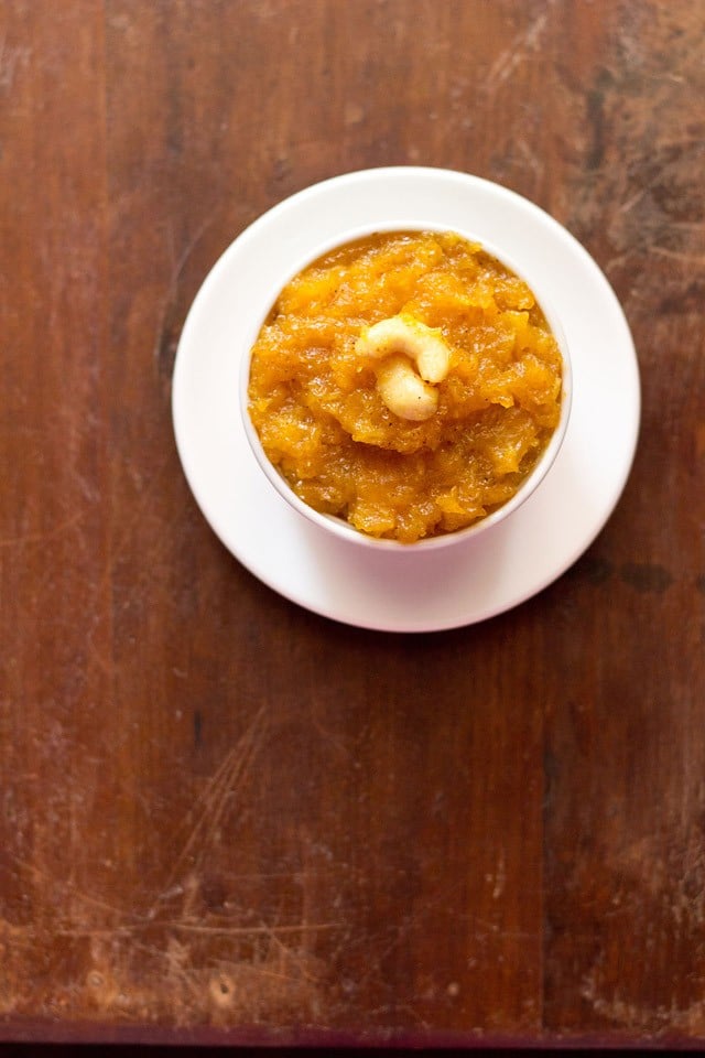 papaya halwa garnished with cashews and served in a white bowl kept on a white plate.