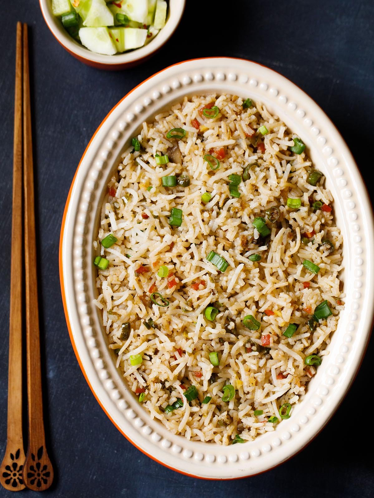 veg fried rice in an oval ceramic bowl with wooden chopsticks on a slate black board