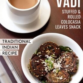 alu vadi garnished with grated coconut, coriander leaves and toasted sesame seeds in a white bowl with a cup of tea kept on the top left side and text layovers.