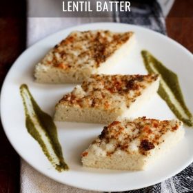 white dhokla cut into diamonds and served with coriander chutney on a white plate with text layovers.