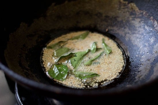 frying mustard seeds, curry leaves, asafoetida and sesame seeds in hot oil for making tempering for alu vadi. 