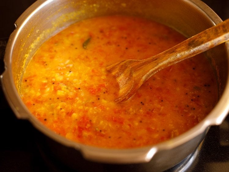 mashing tomato dal with a spoon