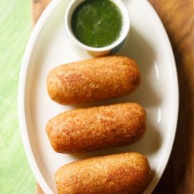 bread roll served on a white platter with a bowl of green chutney kept on the top side.