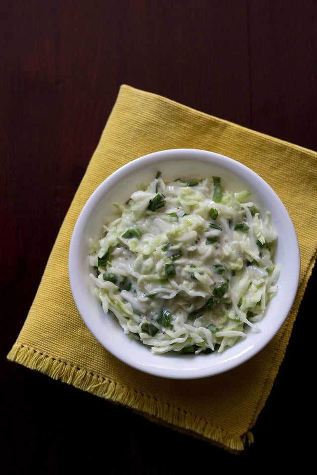 cabbage coleslaw in a white bowl on a yellow napkin on a dark wood table. 