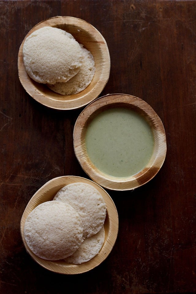 top shot of cooked rice idli served in wooden bowls with coconut chutney in one of the bowls. 