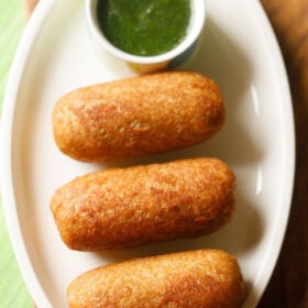 bread roll served on a white platter with a bowl of green chutney kept on the top side.