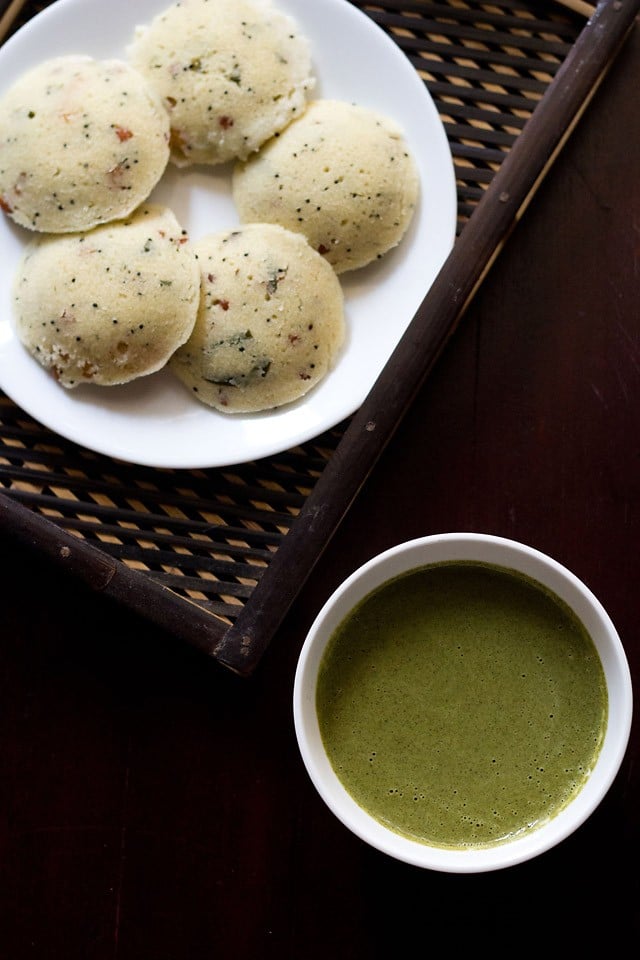 curry leaves chutney served in a white bowl with a plate of idlis kept on the top let side.