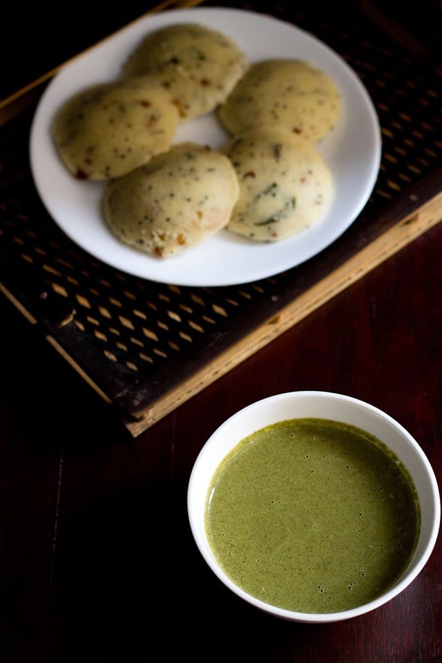 curry leaves chutney served in a white bowl with a plate of idlis kept on the top let side. 