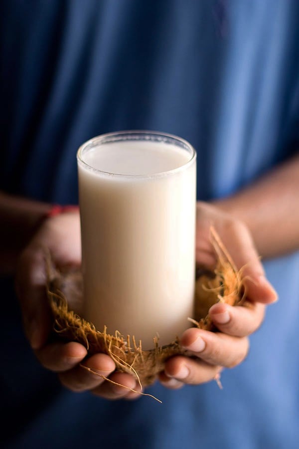 coconut milk served in a glass inside an empty coconut shell being held by hands.