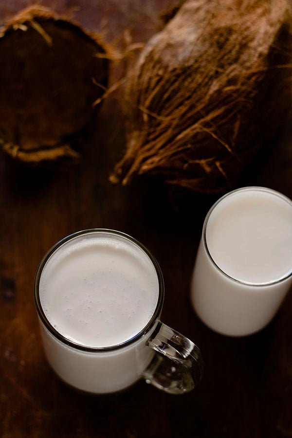 coconut milk served in 2 glasses with coconut husk in the background. 