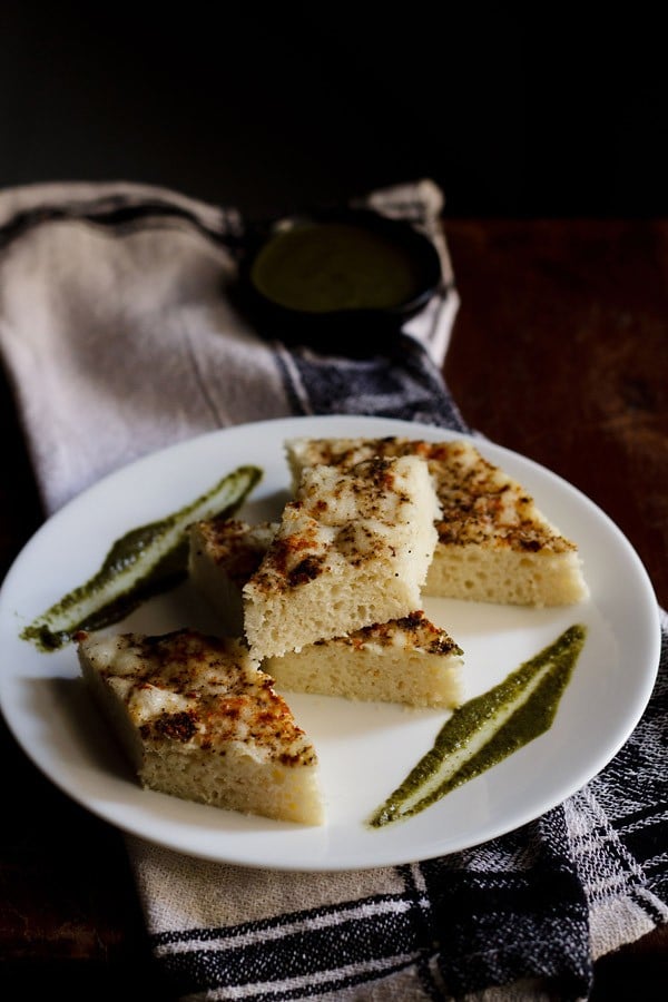 white dhokla cut into diamonds and served with coriander chutney on a white plate. 