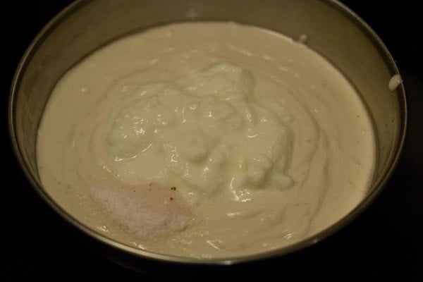 sour curd and salt added to the batter in a bowl for making khatta dhokla. 