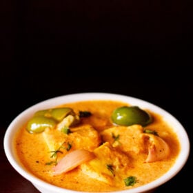 paneer tikka masala served in a white bowl garnished with some coriander leaves on a dark mahogany board.