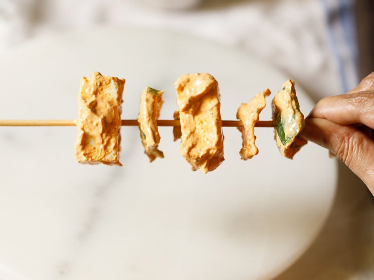 paneer cubes, onion and capsicum being threaded on a bamboo skewer.